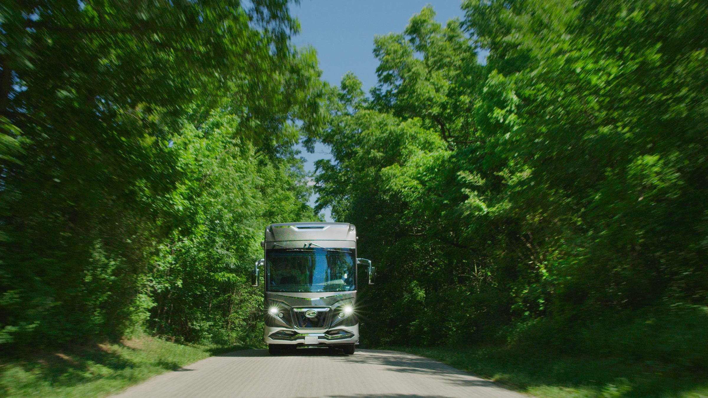 American Coach Rev RV driving on wooded road
