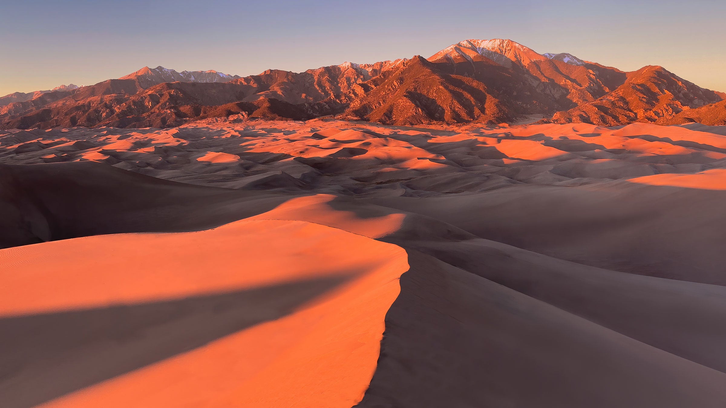 Great Sand Dunes National Park dunefield from the top of the first ridge of dunes. Snow-capped Mount Herard and Cleveland Peak, visible beyond the sea of sand, are part of the Sangre de Cristo Range.